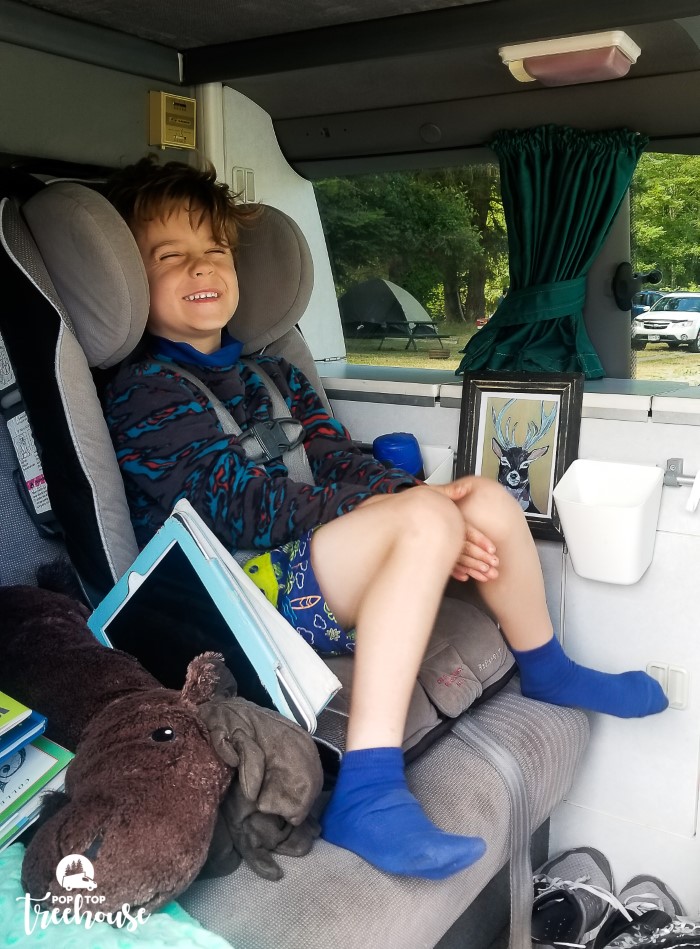 kid in backseat of camper van smiling in a car seat ready for camping